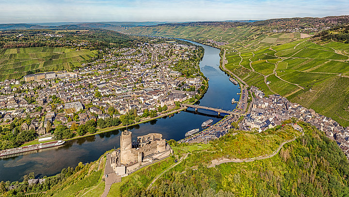 Drohnenbild von der Burg Landshut. Der Blick geht auf die Stadtteile Kues und Bernkastel, die von der Mosel getrennt sind. Umrahmt wird das Bild von Weinbergen.