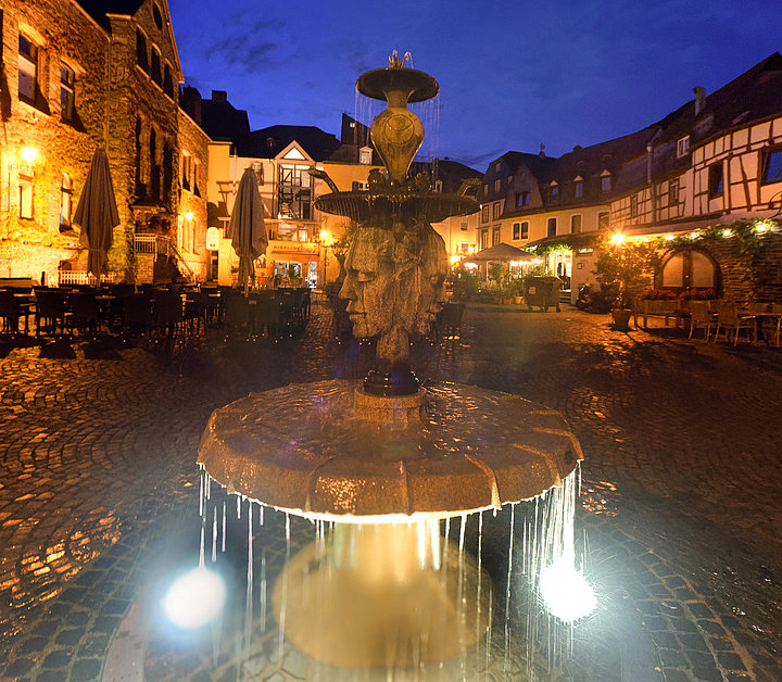 Das Bild ist eine Nachtaufnahme und zeigt den Brunnen auf dem Karlsbader Platz. Der Brunnen des tschechischen Künstlers Jan Kotek auf dem Karlsbader Platz ist ein Geschenk der Partnerstadt von Bernkastel-Kues, Karlovy vary. Die Plastik symbolisiert das ewige Leben, den Tag und die Nacht.