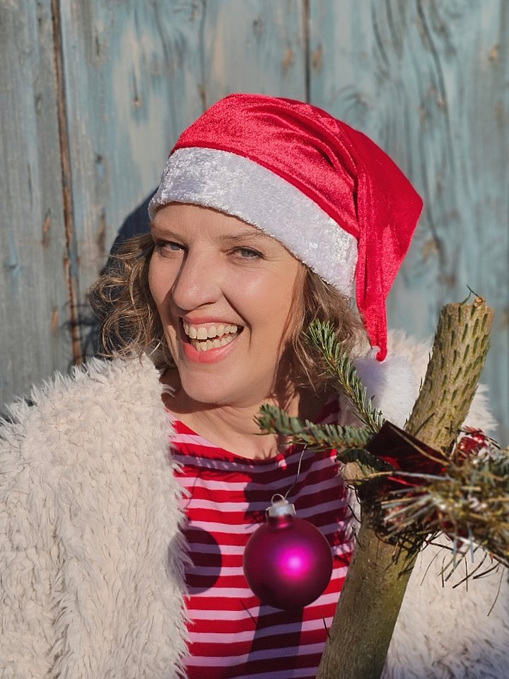 Frau mit blonden Locken, Nikolausmütze und Tannenast mit Weihnachtsbaumkugel