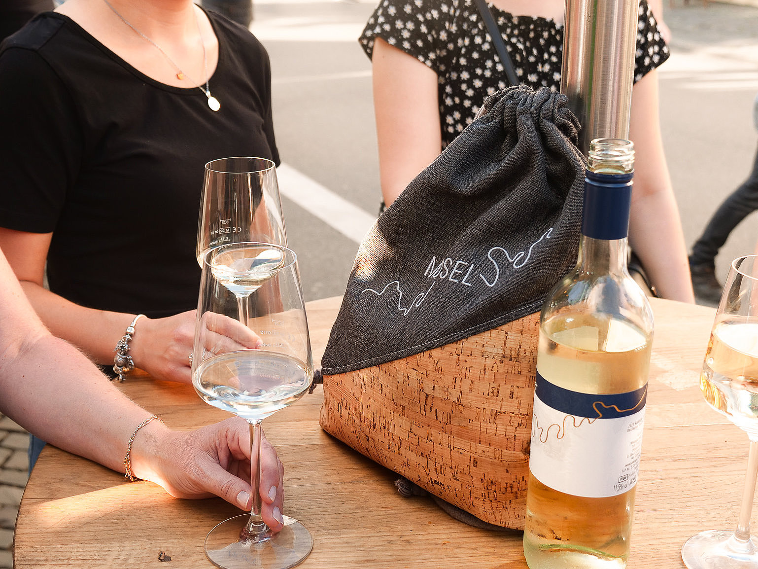 Weingenuss und Geselligkeit auf dem Weinfest der Mittelmosel in Bernkastel-Kues Das Foto zeigt Personen, die an einem Tisch stehen und Wein trinken. Auf dem Tisch ist eine Weinflasche und ein Turnbeutel mit der Aufschrift Moselliebe zu sehen.