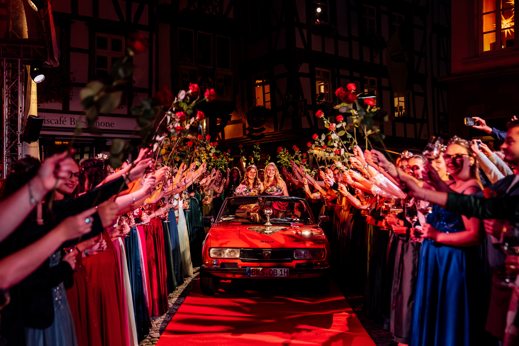 Empfang der Mosella am Weinfest der Mittelmosel in Bernkastel-Kues. Weinhoheiten aus den Moselorten stehen links und rechts entlang eines roten Teppichs Spalier und halten Rosen in der Hand. In der Mitte kommen auf einem roten Oldtimer die Mosella und Weinprinzessin von Bernkastel-Kues eingefahren.